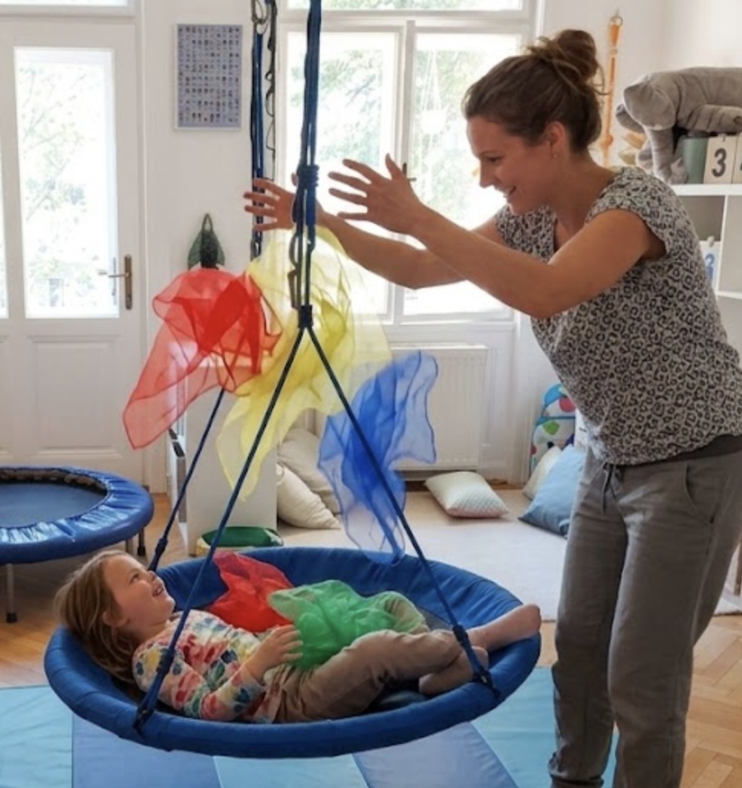 Ergotherapie mit einem Kind in einer Schaukel und bunten Tüchern